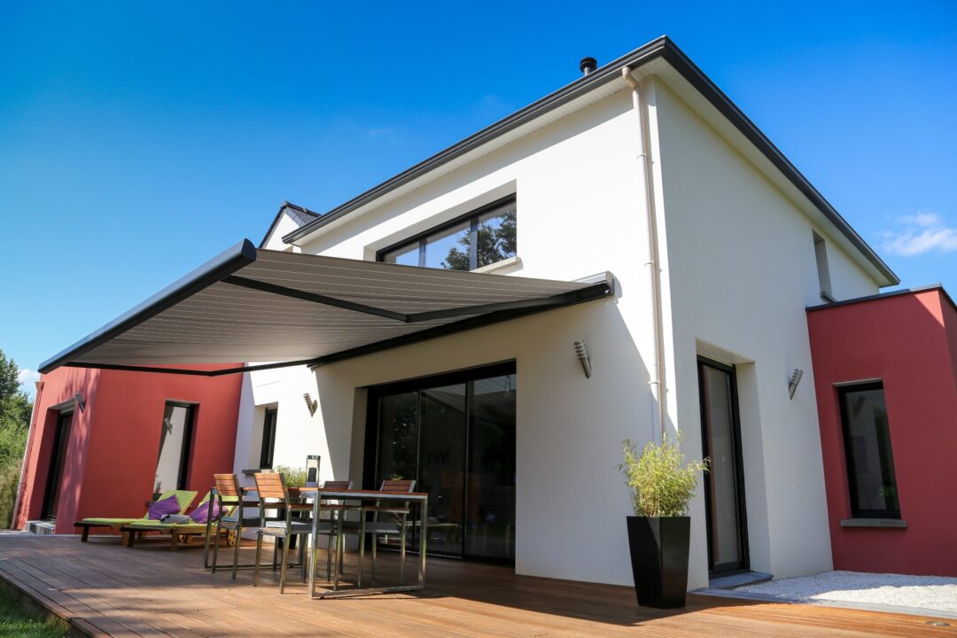 Fotoaufnahme von Aussen eines Hauses mit Terrasse, welche von einem Storen von der Sonne geschützt ist.